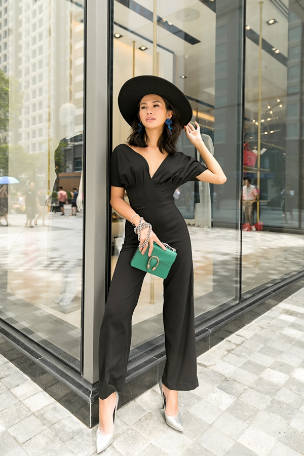 Jumpsuit đen làm nổi bật vóc dáng và chiều cao 1,75 m của Cindy D. Phần xếp pli cách điệu ở ngực tạo cảm giác nữ tính, quyến rũ. Người mẫu nhấn nhá cho trang phục bằng hoa tai sắc xanh, nón rộng vành và một chiếc túi mini.