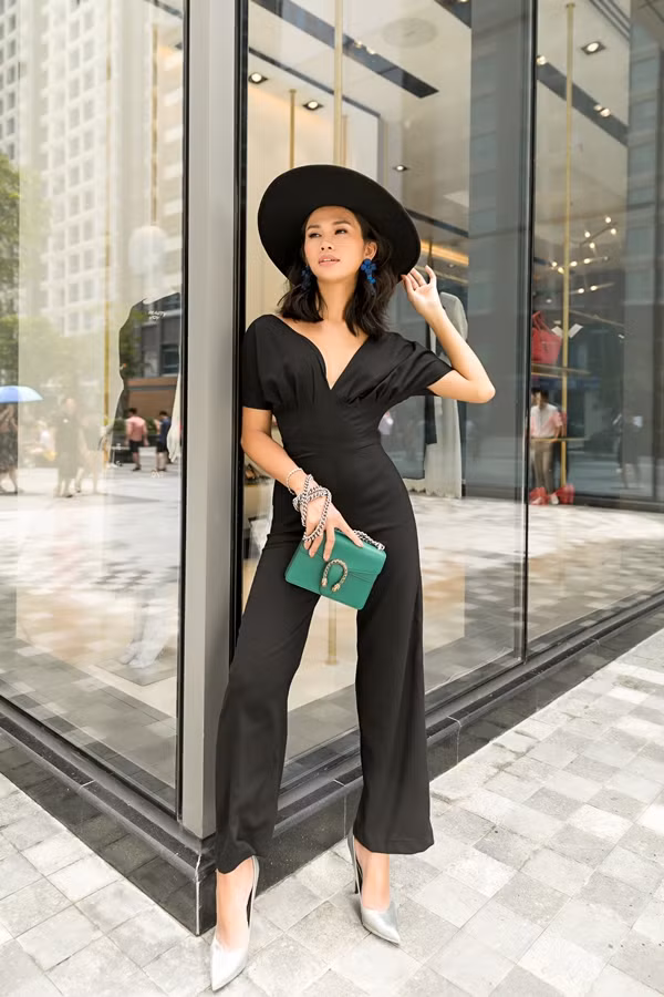 Jumpsuit đen làm nổi bật vóc dáng và chiều cao 1,75 m của Cindy D. Phần xếp pli cách điệu ở ngực tạo cảm giác nữ tính, quyến rũ. Người mẫu nhấn nhá cho trang phục bằng hoa tai sắc xanh, nón rộng vành và một chiếc túi mini.