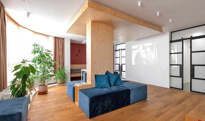 Phòng khách rộng rãi chọn bộ ghế sofa bằng nhung ôm theo trụ đỡ của ngôi nhà, máy chiếu đặt đối diện bức tường màu trắng, cây xanh bố trí men theo khung cửa sổ để lấy ánh sáng và khí trời.