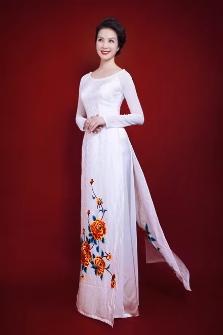 Trong khi áo dài tím và xanh dương toát lên vẻ lộng lẫy thì áo dài trắng cổ thuyền lại đem đến vẻ thanh tao. Phần cổ được đính hạt nhựa trắng, kết hợp hài hòa cùng phần hoa thêu nổi bật phía dưới, giúp bộ áo có những điểm nhấn hợp lý.