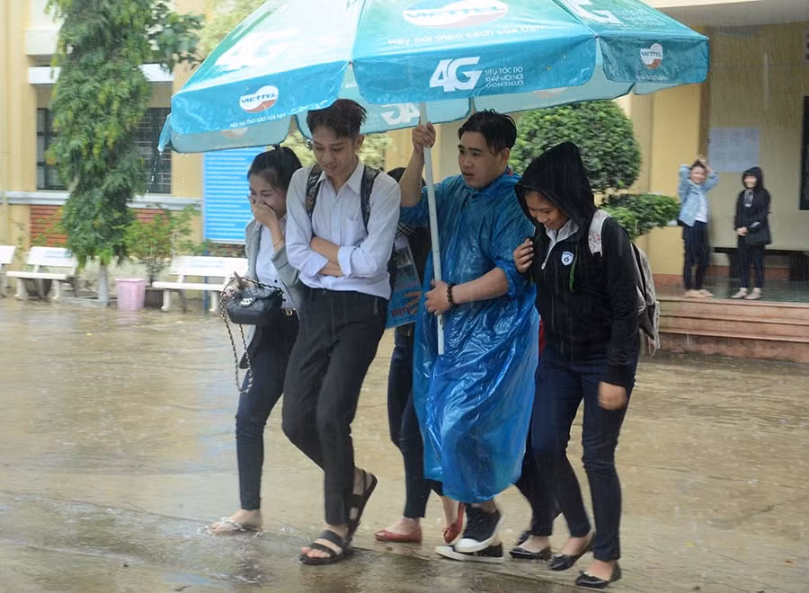 Thành viên đội tiếp sức mùa thi tại Trường THPT Lê Lợi (TP. Pleiku) giúp che mưa cho các thí sinh ra cổng trường sau khi kết thúc môn thi. Ảnh:Phương Vi