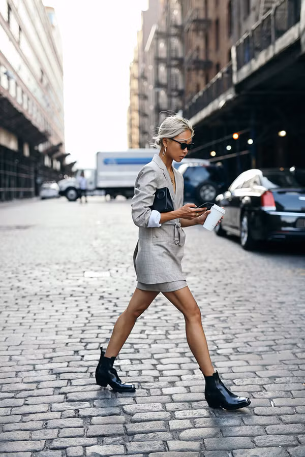 Clutch, bốt cổ thấp tông đen là các món phụ kiện mang lại sự hoàn hảo cho bộ suit xám gồm blazer và chân váy ngắn.