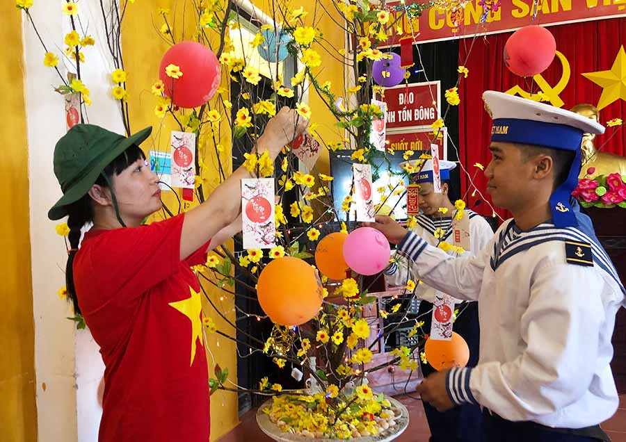  Tác giả (bìa trái) cùng chiến sĩ đảo Sinh Tồn Đông trang trí cây mai đón Tết Kỷ Hợi 2019. Ảnh: Hoàng Thanh Hương