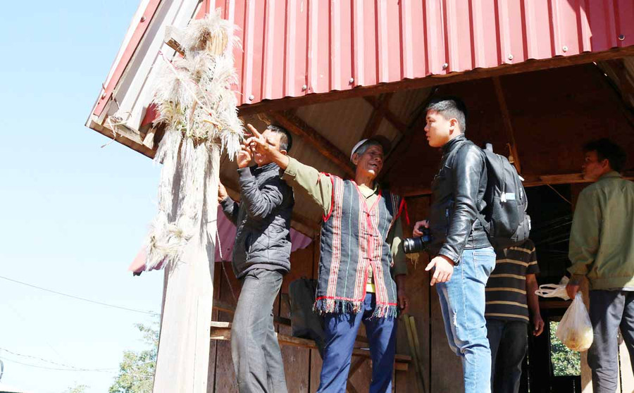 Già Siu Ích hướng dẫn thanh niên trong làng treo bó cỏ lau, một cây ná làm bằng tre bên góc mái hiên nhà rông. Ảnh: Ngọc Sang