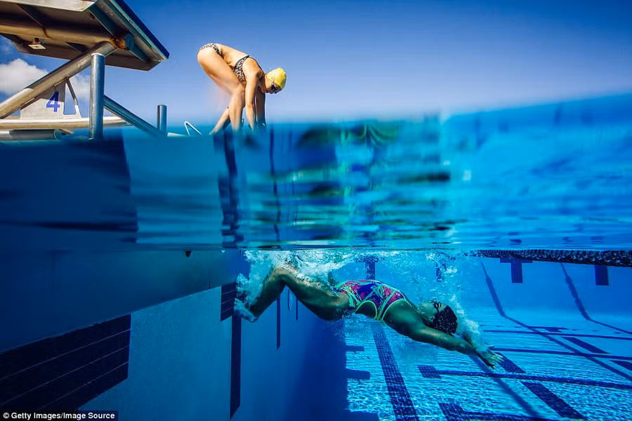 Một người phụ nữ đang bơi trong bể bơi ở Miami (Florida, Mỹ) trong khi người bạn phía trên đang chuẩn bị nhảy xuống bể. Ảnh: Getty Images/Image Source.