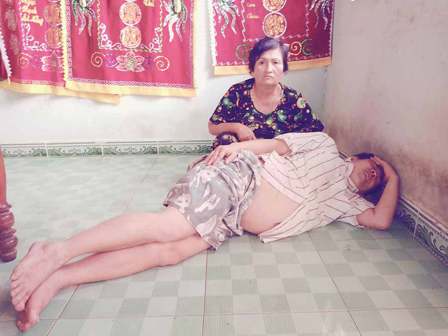 Bà Xi bên người con bị bệnh tâm thần Trương Sơn Đông. Ảnh: Đ.P  Bà Xi bên người con bị bệnh tâm thần Trương Sơn Đông. Ảnh: Đ.P