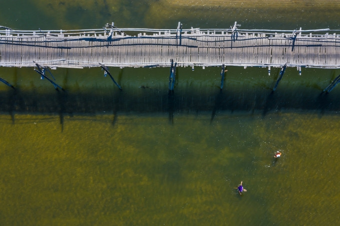 Hai người đang giăng lưới bắt cá gần khu vực cầu Ông Cọp nhìn từ trên cao. Sở hữu vẻ đẹp mộc mạc, hữu tình nên cây cầu gỗ này không chỉ là đường giao thông cho dân địa phương đi lại mà còn là điểm đến của các bạn trẻ, các tay máy săn ảnh.