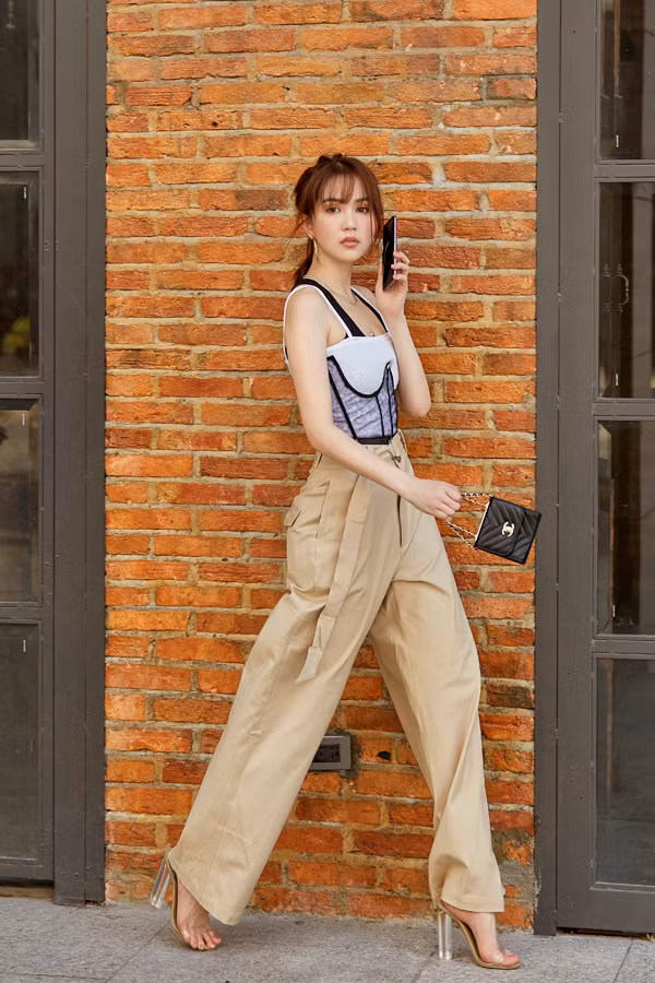 Cảm nhận nhanh nhậy về dòng chảy của xu hướng mới giúp Ngọc Trinh luôn thể hiện rõ tinh thần ăn mặc theo trend. Quần suông vải kaki tông cà phê sữa được cô phối cùng áo hai dây sexy.