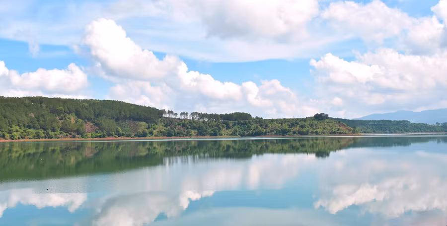 Mây và hàng cây soi bóng xuống mặt hồ.