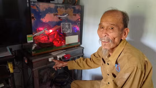  Anh hùng Nguyễn Văn Bảy ấn nút cho mô hình bay mô phỏng lại trận chiến trên không với tấm ảnh chân dung của ông