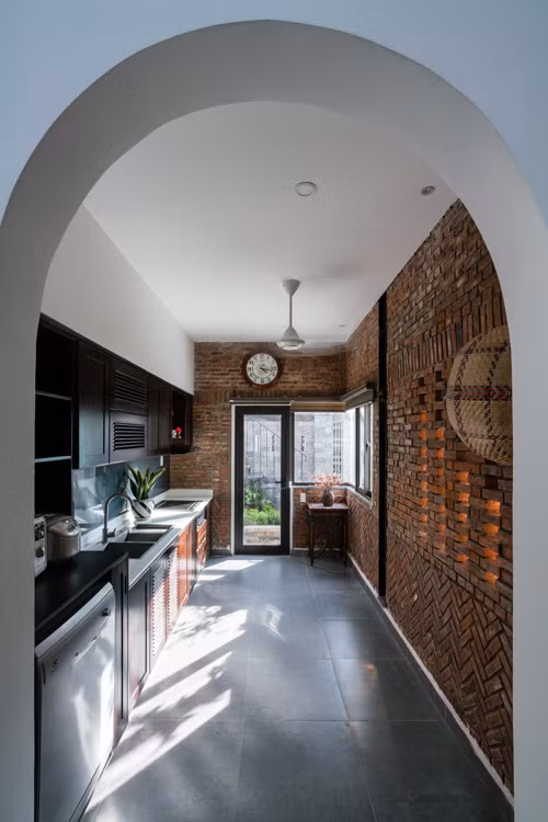  Nhà có hai lối vào từ phòng khách và từ bếp. Khu vực nấu nướng có sự tương phản giữa vật liệu tường gạch mộc với các trang thiết bị hiện đại. Nhưng nhờ tông màu gỗ nâu trầm nên các chi tiết nội thất vẫn có sự kết nối.