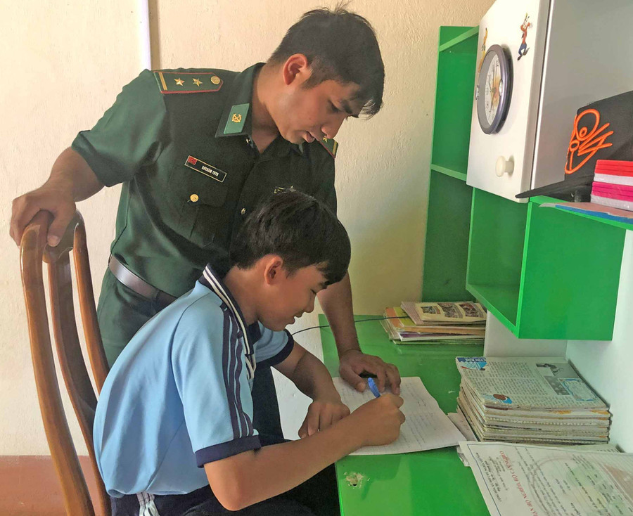 Trung úy Rơ Châm Tuynh hướng dẫn em Nguyễn Quốc Tĩnh-“con nuôi đồn Biên phòng” học bài. Ảnh: Anh Huy
