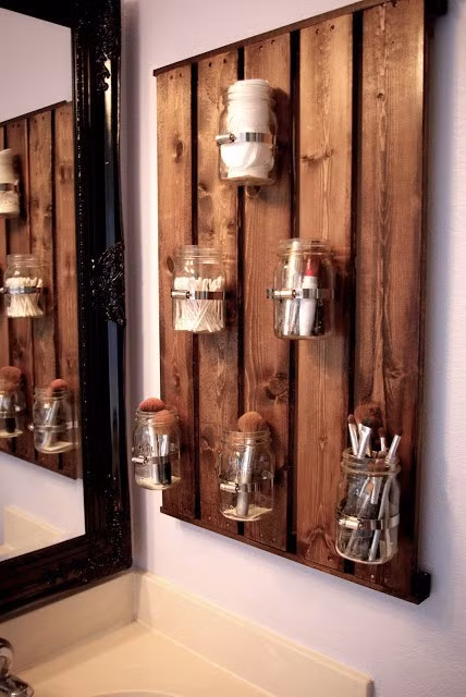 Một bảng mộc trên đó treo các lọ thủy tinh đựng dụng cụ trang điểm vừa có chức năng chứa đồ, vừa có chức năng trang trí đẹp mắt.