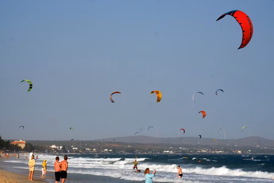 Mũi Né là địa điểm quen thuộc của những người yêu thích các môn thể thao lướt ván nhờ hội tụ nhiều yếu tố như bãi biển đẹp, gió lớn, eo biển có sóng phù hợp để lướt ván. Những ngày nắng đẹp và có gió, những eo biển ở Mũi Né thường rợp bóng diều lướt ván. Ngày 15-3, dù tình hình dịch COVID-19 đang diễn biến phức tạp nhưng cũng không hề khiến bãi biển vắng người chơi lướt ván - Ảnh: SƠN LÂM