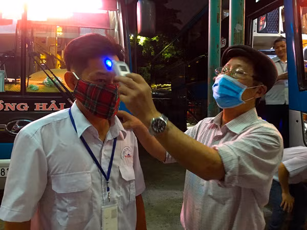 Ông Nguyễn Hồng Hải đo thân nhiệt tài xế trước giờ cho xe khởi hành. Ảnh: H.L