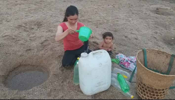Các bà, các mẹ bới cát, đào sẵn những cái hố sâu, rộng trên bãi cát bồi giữa lòng sông chờ cho nước rỉ xuống múc đem về dùng. Ảnh: Vũ Thị Chi