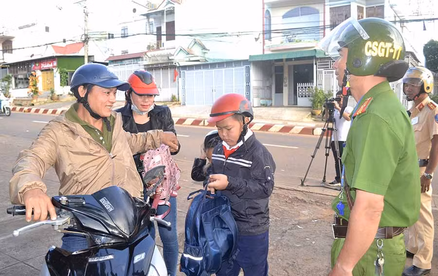 Cảnh sát nhắc nhở một trường hợp chở quá số người quy định khi cha mẹ đưa con tới trường. Ảnh: Lê Hòa
