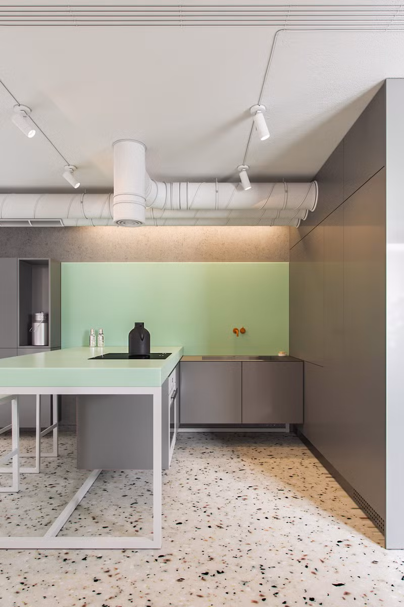 Ống dẫn nước thả từ trần chạm gần với tủ bếp màu xanh mang tạo không gian công nghiệp cho khu vực bếp nấu.