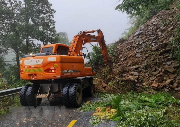  Lực lượng chức năng triển khai phương tiện máy móc tiến hành khắc phục sạt lở đất gây ách tắc giao thông. (Ảnh: TTXVN phát)