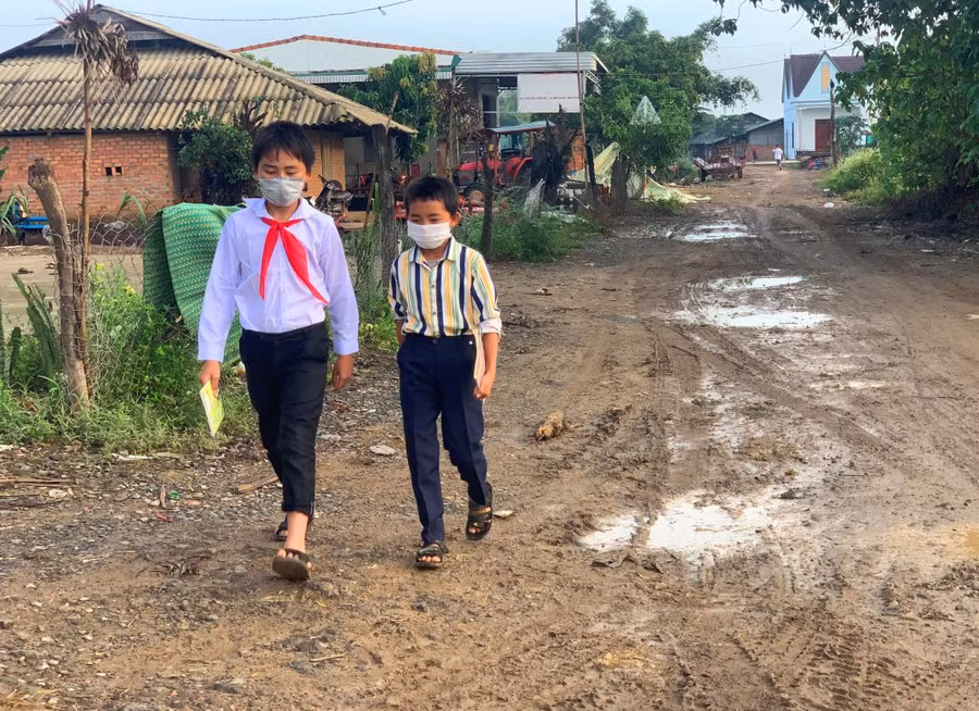 Em Vừ A Phong cùng bạn cắp sách đi bộ trên con đường lầy lội tại làng Mông (xã Nam Ka, huyện Lắk) để đến trường học.