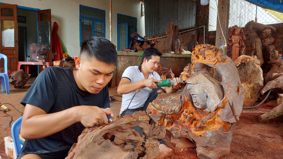 Anh Nguyễn Văn Đức (bìa trái) và Nguyễn Văn Hậu đang chế tác các tác phẩm nghệ thuật từ gỗ lũa. Ảnh: Nguyễn Tú