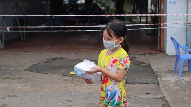  Bé gái tranh thủ ra lấy phần đồ ăn cho mình khi cùng ba mẹ chờ bên đường. Ảnh: Hoàng Giáp