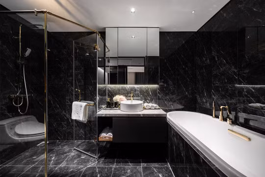 Có thiết kế tương tự căn hộ thông tầng ở Hai Bà Trưng song phòng tắm trong căn hộ thông tầng ở quận Bắc Từ Liêm (Hà Nội) sử dụng nhiều gạch đá đen hơn bởi gia chủ là nam giới. Theo KTS Nguyễn Việt Linh, người thiết kế hai công trình này, gam màu tối giúp phòng tắm trông sạch sẽ và mát mẻ hơn.