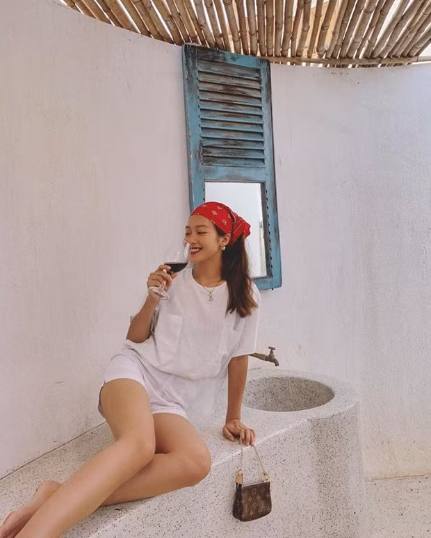 Khả Ngân tận hưởng khoảnh khắc thưởng rượu ở vùng thôn dã. Cô nàng mặc áo thun, quần shorts trắng ton-sur-ton. Chiếc khăn buộc đầu và sắc tay Louis Vuitton được trưng dụng để tạo điểm sáng thú vị.
