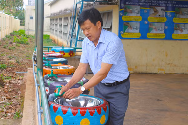 Thầy Nguyễn Trọng Ngoạn-Hiệu trưởng Trường Tiểu học thị trấn Phú Hòa bên những bồn rửa tay tái chế từ lốp xe để phục vụ học sinh trở lại trường. Ảnh: P.L