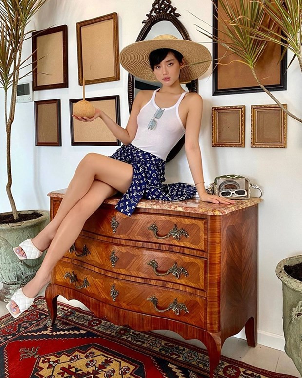 Giữ vững tinh thần dịch chuyển, Khánh Linh biến căn hộ của mình thành khu nghỉ dưỡng riêng. Nàng fashionista diện áo tank, ''F5'' áo pyjama Louis Vuitton thành đồ cover-up. Cô nàng còn trưng dụng mũ cói vàng rộng, mang sandals cao gót, thư giãn ngay trong chính phòng khách nhà mình.