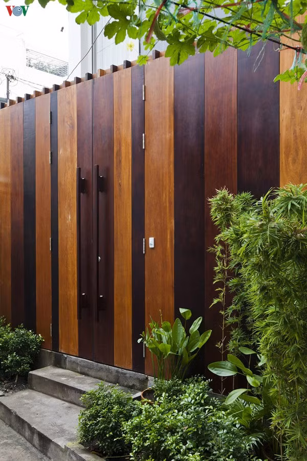 Kiến trúc sư đã có một lời giải hợp lý cho bài toán khó, đáp ứng được những nhu cầu của chủ nhà. Vì ngõ nhỏ nên để kín đáo, cổng sử dụng mảng đặc, nhưng vẫn thân thiện nhờ chất liệu gỗ và những chậu cây xanh phía trước.