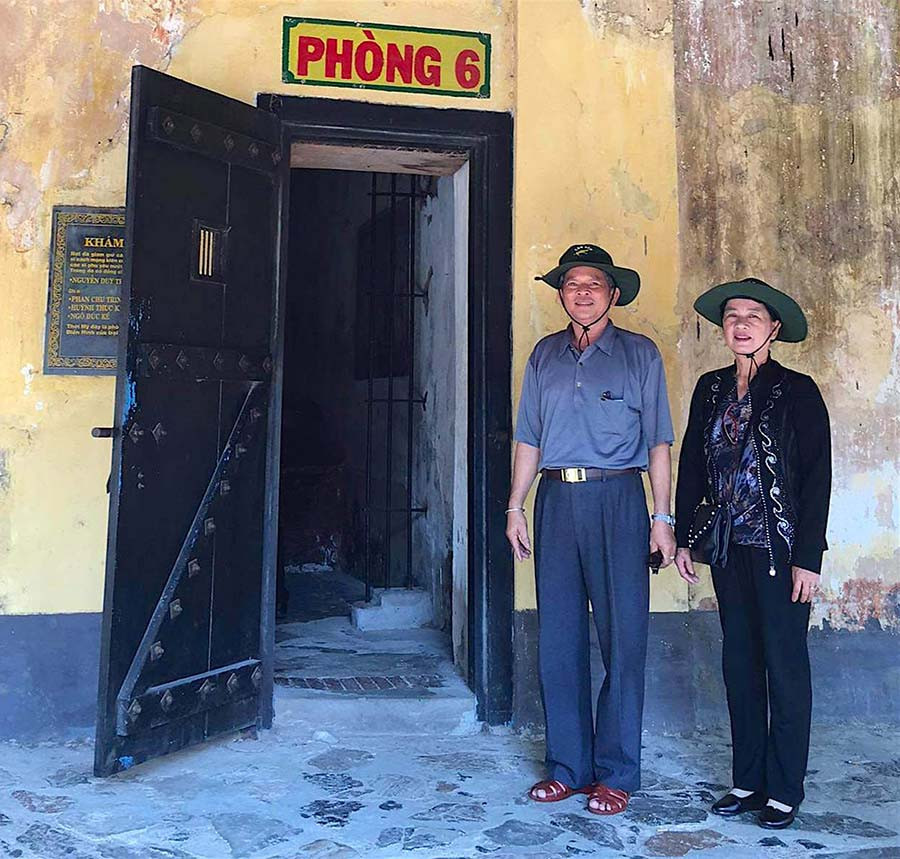 Vợ chồng bà Cúc chụp ảnh lưu niệm trước căn phòng nơi bà từng bị giam giữ tại Côn Đảo (Ảnh nhân vật cung cấp).