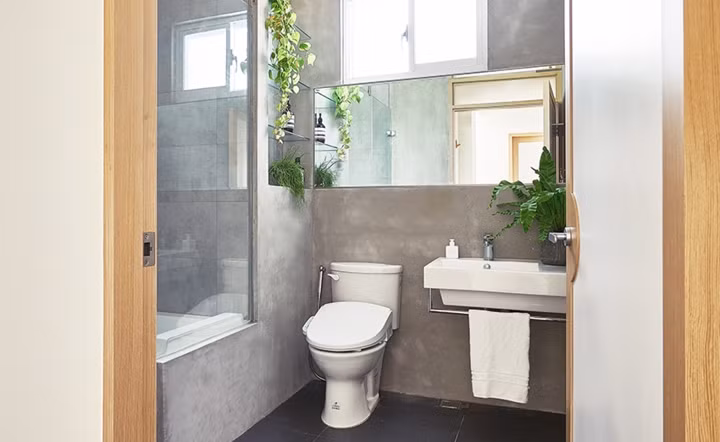 Phòng tắm được chia thành hai khu vực khô và nước với những mảng tường bê tông xám kết hợp các thiết bị màu trắng tinh tế.