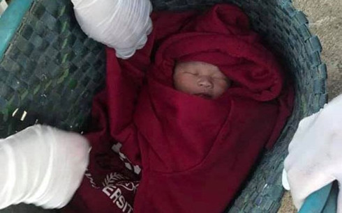 Bé trai sơ sinh được quấn trong chiếc áo ấm màu đỏ và để trong chiếc túi màu xanh, bỏ trước nhà một người dân.