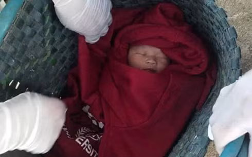 Bé trai sơ sinh được quấn trong chiếc áo ấm màu đỏ và để trong chiếc túi màu xanh, bỏ trước nhà một người dân.