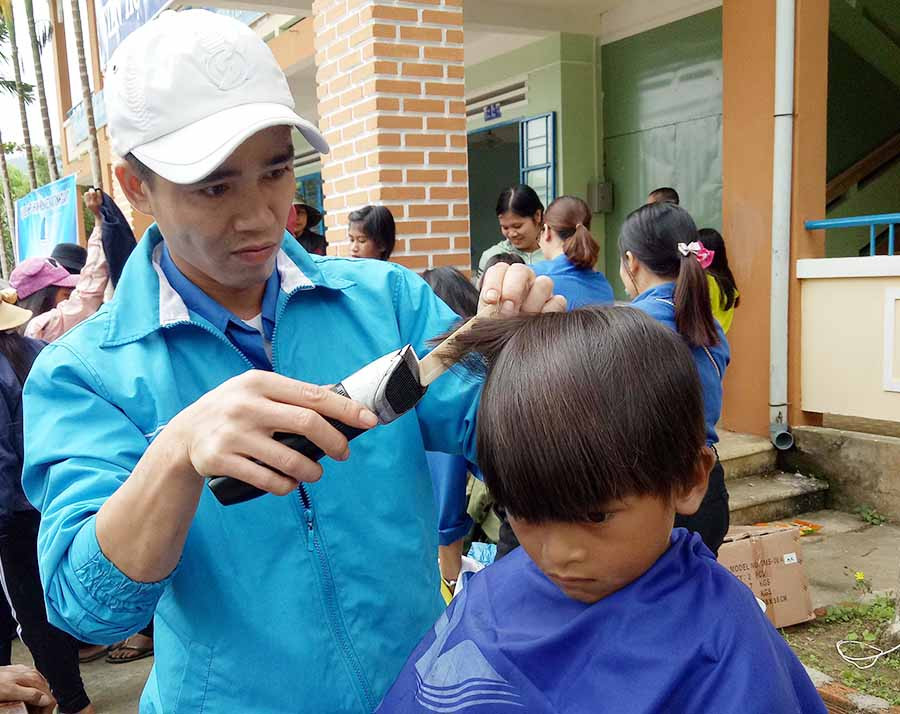  Một thành viên trong đoàn cắt tóc cho các em học sinh. Ảnh: P.L