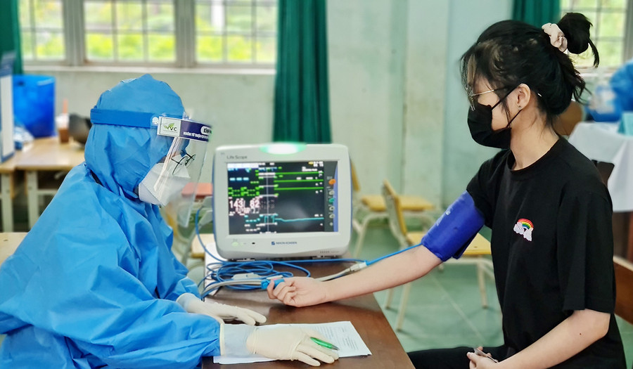 Nhân viên y tế kiểm tra sức khỏe của học sinh trước khi tiêm phòng Covid-19. Ảnh: Bá Bính