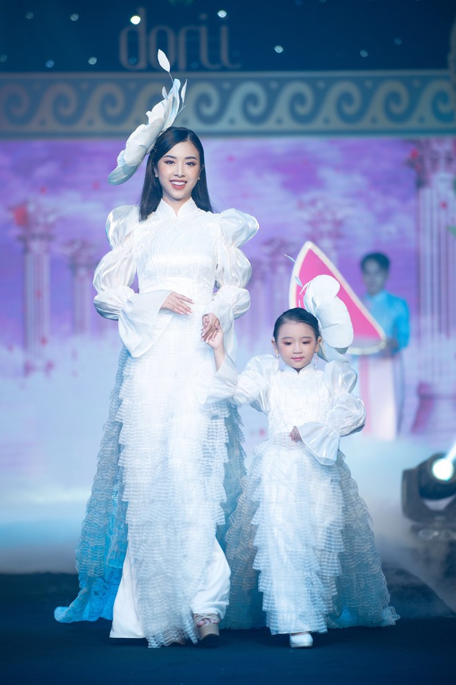 Á hậu Thúy An mang đến một phong cách hoàn toàn khác so với các đồng nghiệp. Á hậu 2 Hoa hậu Việt Nam 2018 rạng rỡ trong tà áo dài màu trắng được cách điệu ở phần tay và phần tà áo. Đồng hành cùng cô là người mẫu nhí Tô Hồng Yến Oanh. ẢNH: NGUYỄN XUÂN HUY