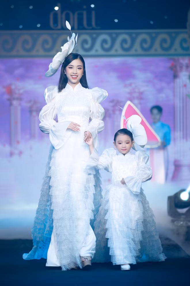 Á hậu Thúy An mang đến một phong cách hoàn toàn khác so với các đồng nghiệp. Á hậu 2 Hoa hậu Việt Nam 2018 rạng rỡ trong tà áo dài màu trắng được cách điệu ở phần tay và phần tà áo. Đồng hành cùng cô là người mẫu nhí Tô Hồng Yến Oanh. ẢNH: NGUYỄN XUÂN HUY