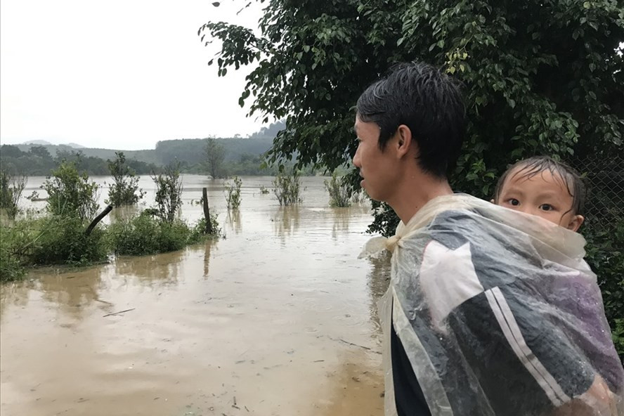 Một người dân xã Cư San, cõng con sau lưng, trùm áo mưa đứng lặng nhìn ra phía lòng hồ Krông Pách thượng - nơi nước lũ đang dâng cao sau bão số 12. Ảnh: Bảo Trung Một người dân xã Cư San, cõng con sau lưng, trùm áo mưa đứng lặng nhìn ra phía lòng hồ Krông Pách thượng - nơi nước lũ đang dâng cao sau bão số 12. Ảnh: Bảo Trung