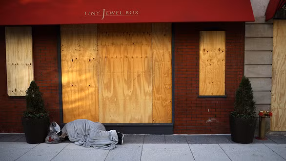 Một người vô gia cư nằm bên ngoài một cửa hàng được che chắn bằng ván ép ở thủ đô Washington ngày 3-11 để đề phòng bạo lực hậu bầu cử - Ảnh: Reuters