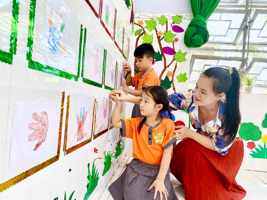 Giáo viên Trường Mẫu giáo Hoa Mai hướng dẫn các bé trưng bày tác phẩm trải nghiệm, sáng tạo của mình tại lớp học. Ảnh: Mộc Trà