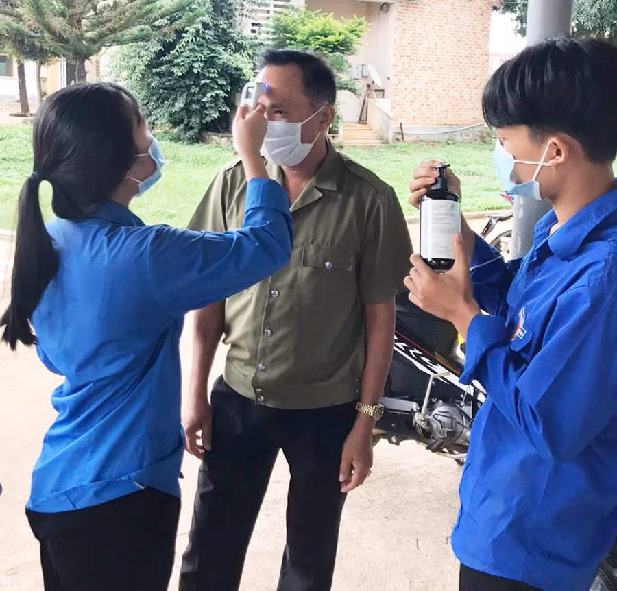  Đoàn viên, thanh niên tiến hành đo thân nhiệt cho người dân khi đến trụ sở UBND thị trấn đăng ký làm việc. Ảnh: Hà Phương