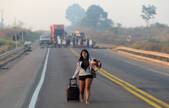 Một phụ nữ đang đi trên đoạn quốc lộ BR 163 của Brazil đã bị các thổ dân Kayapo chặn lối khi họ biểu tình chống lại các biện pháp mà chính quyền áp đặt để tránh sự lây lan của COVID-19 ở Novo Progresso, bang Para, Brazil ngày 17-8 - Ảnh: REUTERS  Một phụ nữ đang đi trên đoạn quốc lộ BR 163 của Brazil đã bị các thổ dân Kayapo chặn lối khi họ biểu tình chống lại các biện pháp mà chính quyền áp đặt để tránh sự lây lan của COVID-19 ở Novo Progresso, bang Para, Brazil ngày 17-8 - Ảnh: REUTERS