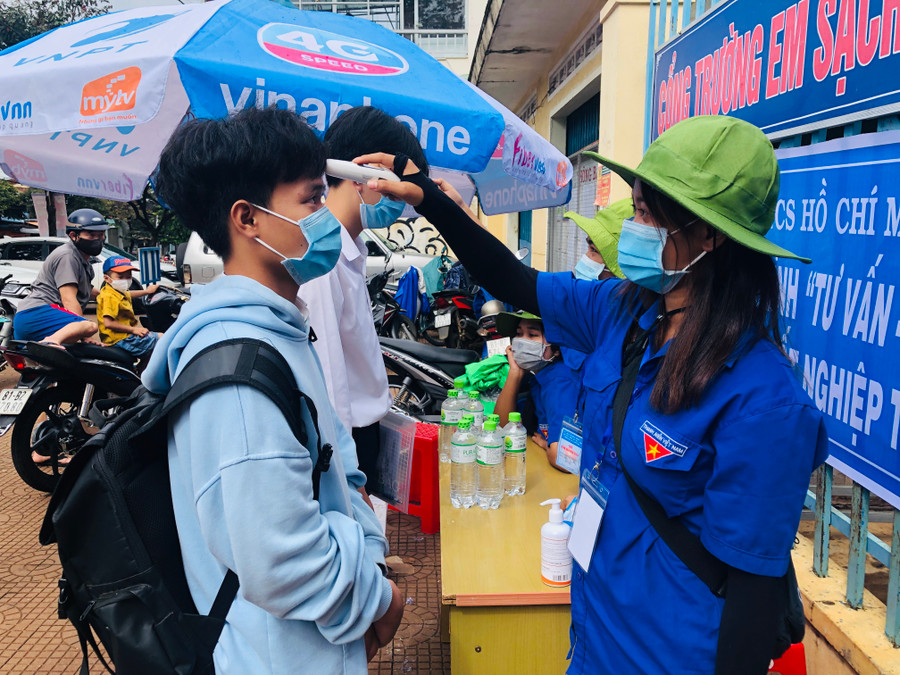Tình nguyện viên hỗ trợ đo thân nhiệt cho các thí sinh trước khi vào điểm thi. Ảnh: Thủy Bình Tình nguyện viên hỗ trợ đo thân nhiệt cho các thí sinh trước khi vào điểm thi- Ảnh TB