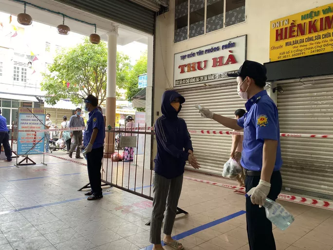 Bảo vệ xịt khử khuẩn và đo thân nhiệt cho người đi chợ