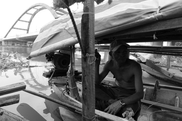 Ngày trước, khi cá tôm còn nhiều các gia đình đều mưu sinh dựa vào việc đánh bắt tôm cá. Sau này, tôm cá ít nên ngoài việc đi đánh bắt, họ phải làm đủ thứ nghề để mưu sinh. Trong ảnh: Ông Nguyễn Văn Minh (55 tuổi) đang ngồi trên ghe chờ đi chở hàng thuê cho khách.