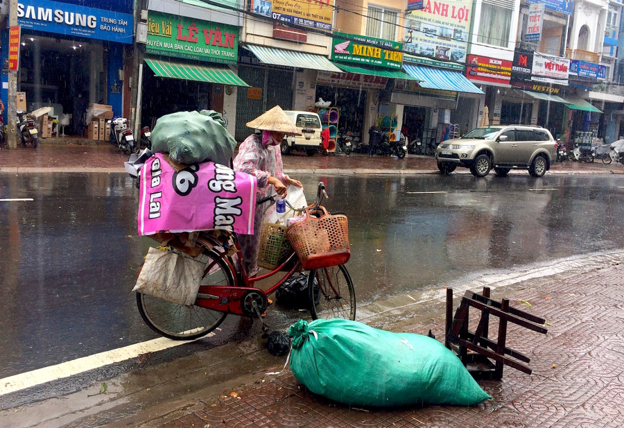 Bà Cúc nhặt nhạnh ve chai bên đường dưới cơn mưa như trút nước. Ảnh: Hồng Thi