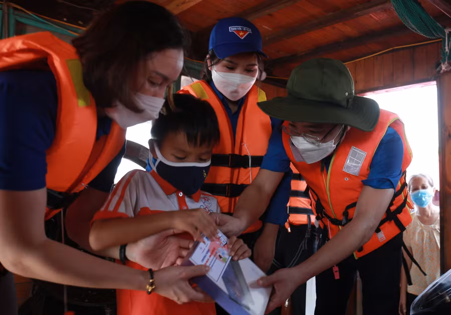 Anh Nguyễn Tường Lâm (phải) và chị Chu Hồng Minh (giữa) trao tặng máy tính bảng cho trẻ em ở làng chài ven sông Hồng. Ảnh: Bảo Anh
