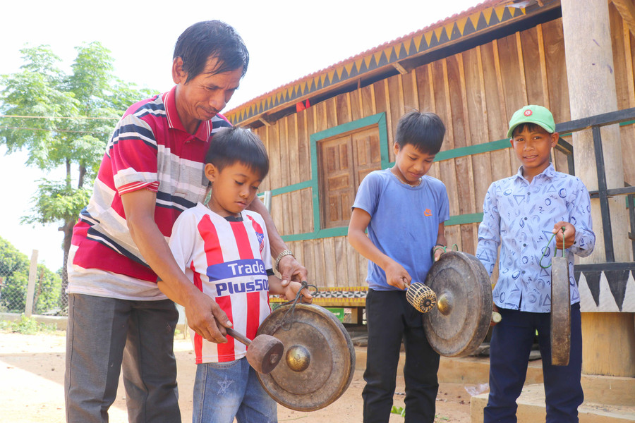 Thiếu niên làng Bờ-Chư Pâu được nghệ nhân trong làng tận tình hường dẫn cách đánh cồng chiêng. Ảnh: Ngọc Minh 